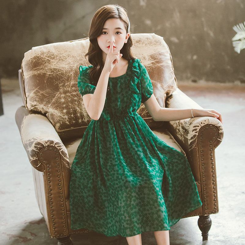 Little girl wearing a green summer chiffon skirt, sitting on a cushioned chair.