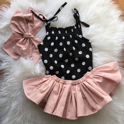 Baby girls polka dot strap shirt with pink skirt clothing set on fluffy surface.