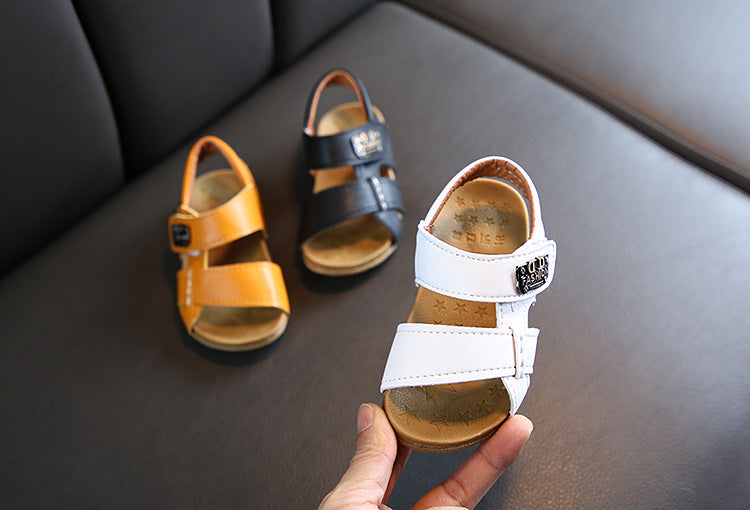 Baby girls microfiber leather sandals in white, black, and yellow on a couch.