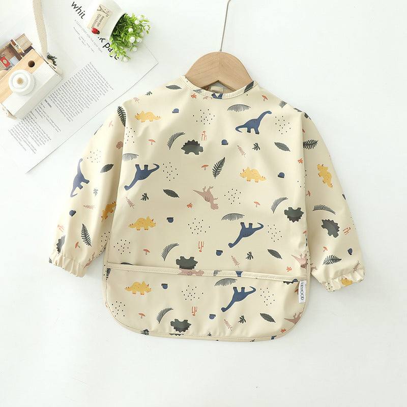 Children's waterproof cartoon feeding coat with pockets in beige, dinosaur pattern.