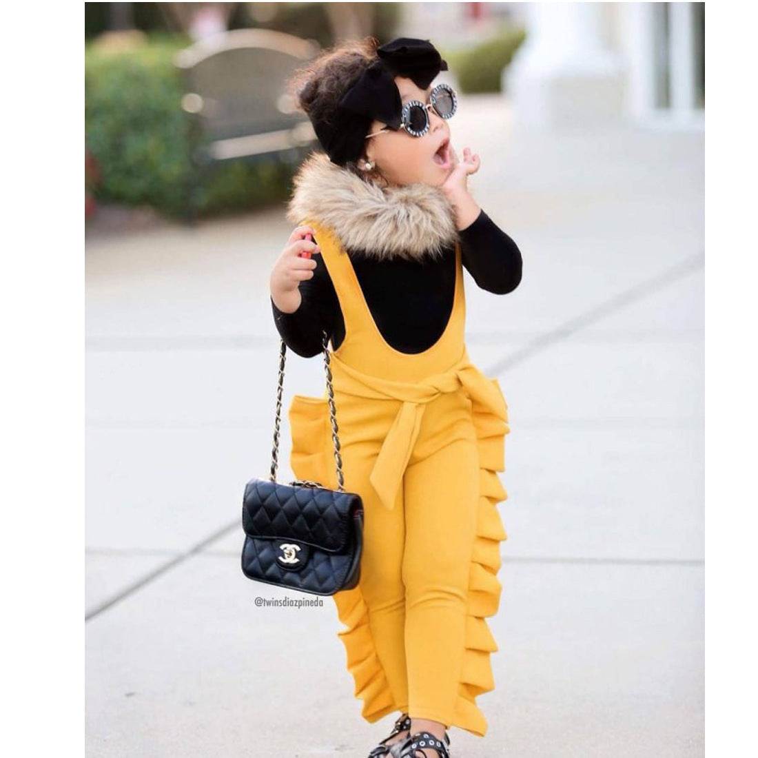 Child wearing stylish yellow cotton overalls with ruffle sides, accessorized with sunglasses and a purse.