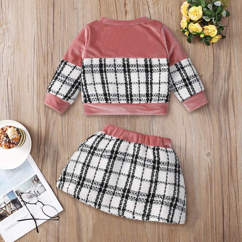 Plaid print baby girl skirt set with pink long sleeve top on a wooden background.