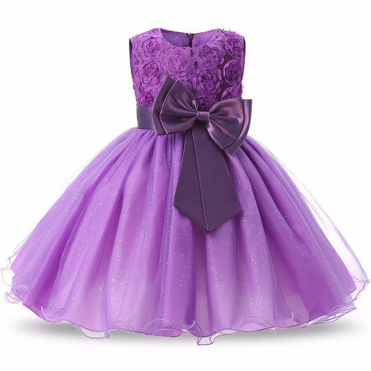 Knee-length purple girls' pageant dress with floral decoration and bow, sleeveless A-line silhouette.