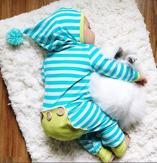 Baby wearing striped long sleeve hooded onesie on fluffy carpet.